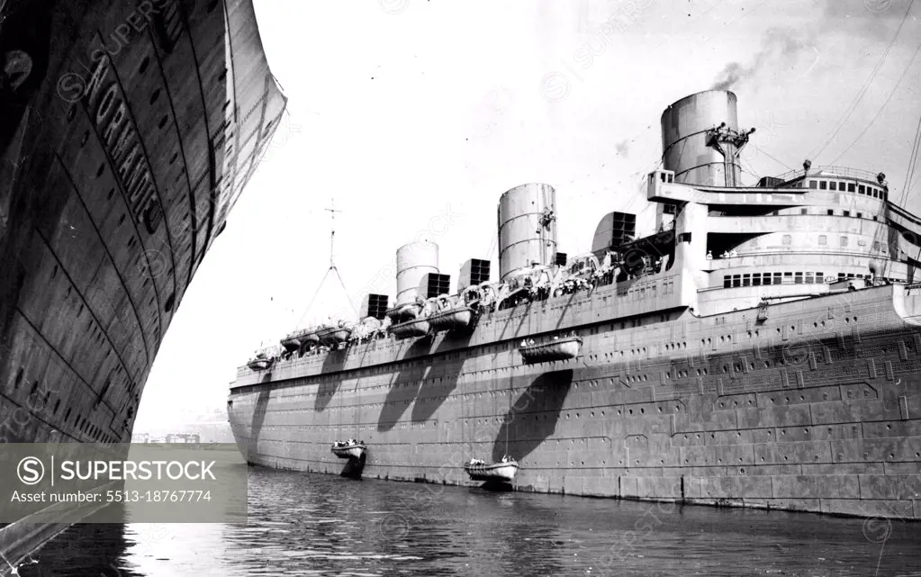 Queen Mary Preparing For Mystery Voyage -- Lifeboats being lowered into the water from the Queen Mary at her pier in New York today as preparations were made for quick departure. The Queen Mary received a large addition to her crew on Monday when 770 seamen arrived here on the S.S. Antonia and were divided between the Queen Mary and the Mauretania. In this photo the new crew members are operating the lifeboat mechanisms. No information has been given out by the Cunard white star line on the trip contemplated for the two giant liners. In the foreground is shown the S.S. Normandie sow of the French line. March 20, 1940. (Photo by Wide World Photo).