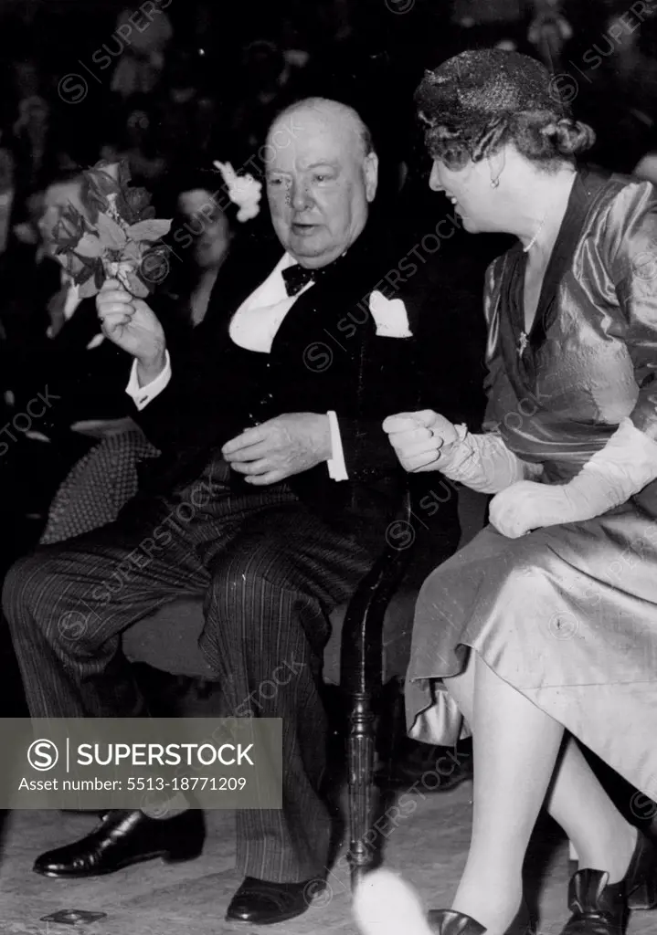 Floral Touch -  Prime Minister Sir Winston Churchill clutches a bouquet presented him by children at the Royal Albert Hall, during a mass meeting held in conjunction with the 27th Conservative Woman's Annual Conference. The Premier addressed the meeting. Seated next to him is Mrs. Walter Elliot, Vice-Chairman 1953-54. May 27, 1954. (Photo by United Press Photo).