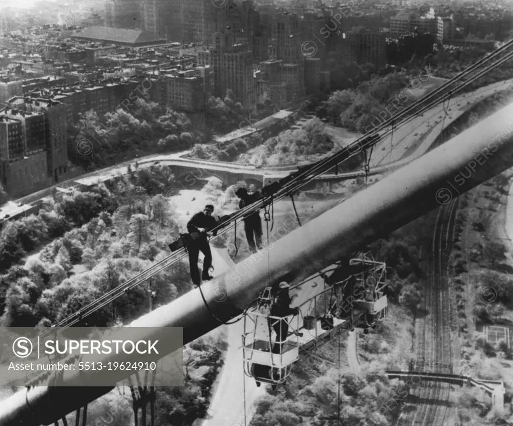 Spring Cleaning -- Painters using an electrically operated scaffold, called "spider staging," work on a cable high above the Manhattan side of the George Washington Bridge as part of a force of 50 carefully picked workmen who yesterday started a two-year painting job. The project will cost $150,000, including $35,000 for 11,000 gallons of paint. In background are apartment buildings along Riverside Drive, and below the workmen are the West Side Highway and the New York Central Railroad tracks. May 08, 1954. (Photo by AP Wirephoto).