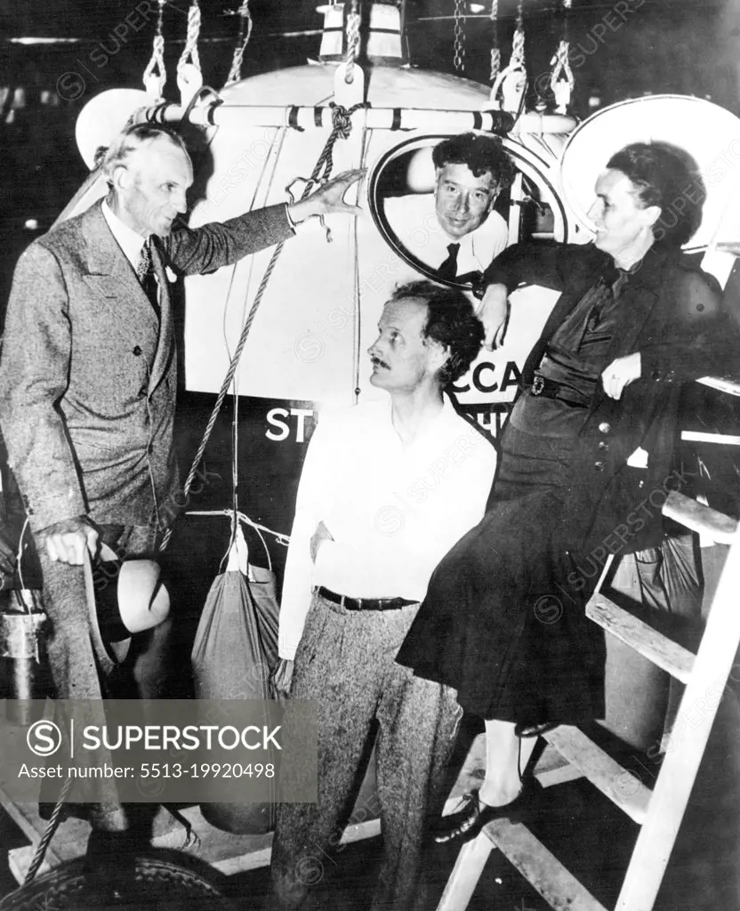 Ford Chats With Flying Piccards -- Henry Ford, automobile manufacturer, (left) chatted with Dr. and Mrs. Jean Piccard at Ford Airport, Detroit, while waiting for the start of the projected stratospheric flight early on the morning of Oct 13. Prof. W.F.G. Swann, of the Franklin Institute, Swarthmore, PA., can be seen looking through a Porthole of the Gondola in which the Piccards plan to ride high into the stratosphere. A few minutes after this picture was taken, the Filght was postponed because of high winds. October 13, 1934. (Photo by Associated Press Photo).