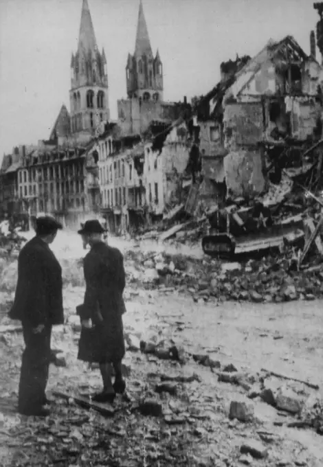 Church Spires Survive Bombardment -- Two French civilians gaze at the twin spires of a church in Caen, France, which stand almost unscathed amid the wreckage of surrounding buildings badly damaged by heavy barrage which preceded the downfall of the former German strongpoint in Normandy. December 07, 1944. (Photo by Associated Press Radiophoto).