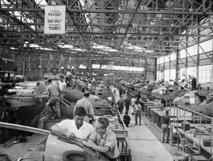 Wants To Advance -- Kenneth McMahon, (Right) talks over a detail of the manufacture of airlines at the Lockheed plant, Burbank, Cal., with Todd Oviatt, his superior. He hopes by successive "Upgradings" eventually to step into a supervisor's shoes. That's why he has been spending a couple of nights a week in study. Scene inside one of the great construction hangars of the Lockheed Aircraft Corporation at Burbank, California. July 20, 1941. (Photo by Associated Press Photo).