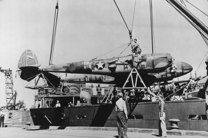 New U.S. Planes Arrive In Australia -- A P-38 "Lightning" is unloaded on a pier somewhere in Australia, one of a recent large shipment to arrive there from the U.S. The P-38's are rated with the best high altitude interceptor and fighter planes in the world, attaining a speed in excess of 400 miles per hour. It is a twin-motored plane with the main armament mounted in the center fuselage section. February 08, 1943. (Photo by Interphoto News Pictures, Inc.).