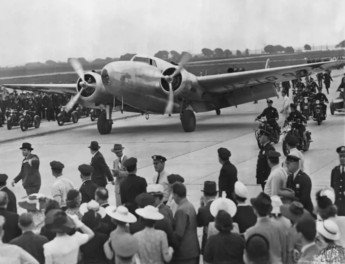 Hughes Completes The Globe Circle -- Here's the world-girdling silver Monoplane of the Howard Hughes round-the-world flight as it taxied into Floyd Bennett Airport, New York City, July 14. A throng of excited New Yorkers were on hand to greet the five inspired airmen aboard. July 14, 1938. (Photo by Associated Press Photo).