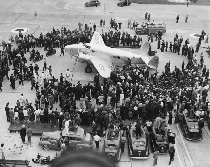 Ring Around An Airsteed -- Howard Hughes twin-motored Monoplane is shown on the concrete apron at Floyd Bennett Airport, July 14, at the end of the flight around the world. Moviemakers Newsmen and officials comprise the crowd. July 14, 1938. (Photo by Associated Press Photo).