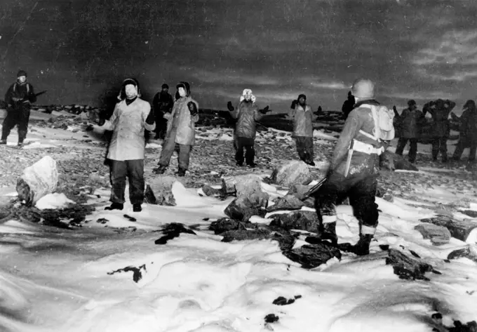 Germans Captured on Greenland: Coast guardsmen guard a group of German prisoners who raise their hands in surrender following their capture during recent action on Greenland. The Germans were attempting to establish and maintain radio-weather stations in the area. The coast guardsmen accounted for the capture of 60 German prisoners, destruction of two enemy bases, capture of a new armed trawler and the scuttling of another with a third abandoned in the ice. December 14, 1944. (Photo by Associate