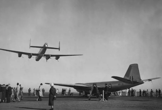 First Australian-Built Canberra Jet Bomber stands on the Avalon airstrip near Geelong today before its first official flight. Overhead an Australian built Lincoln bomber demonstrates flying on one engine. The propeller second from the right is the only one rotating. June 29, 1953.