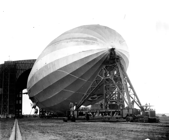 Testing Navy's New Portable Mooring Mast The U.S.S. Los Angeles, hooked to the new portable mooring mast, leaves the hangar here as the mast is drawn gut upon the field by a tractor preparatory to testing the new facilities which the new apparatus offers for landing as well as launching. The portable mast passed the test satisfactorily and is said to mark a real development in hangar equipment since it greatly decreases the number of men required to assist in the "take-off." May 26, 1930. (Photo