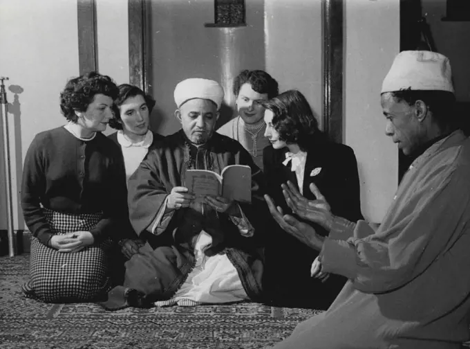 In a mosque in Cardiff's dockland, four British converts to the Moslem faith listen as the Imam of the mosque, Abdulla-El-Hakin, reads to them from the Koran - the Moslem Bible. Kneeling on the right is Ali Mohammad, one of the Mosque dignitaries. Scenes like this are not unusual in Cardiff. The Arabs in Tiger Bay - the dockland area - number 3,000, forming the largest Moslem community in Britain. Many of them marry Christian girls, and in most cases when that happens the girls adopt the faith o