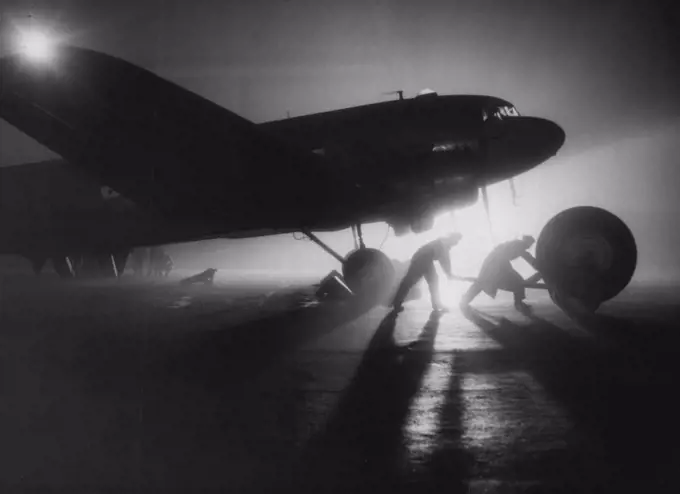 Backing Up The "Air-Lift" -- Honington is busiest at night, when aircraft are loaded so that at first light they may take off for bases in Germany. Here a giant wheel for a York aircraft, grounded at Wunstorf, Germany, is trundled out to a waiting Dakota of "Operation Plumber." An important if unspectacular link in the maintenance of the Royal Air Force's contribution to the "Air-Lift" into blockaded Berlin is "Operation Plumber." This is the R.A.F.'s name for the major servicing unit of transport Command at Honington, Suffolk, where a fleet of six Dakota are kept busy flying unserviceable aircraft parts back from Germany and taking out immediate replacements. November 24, 1948. (Photo by Associated Press Photo).