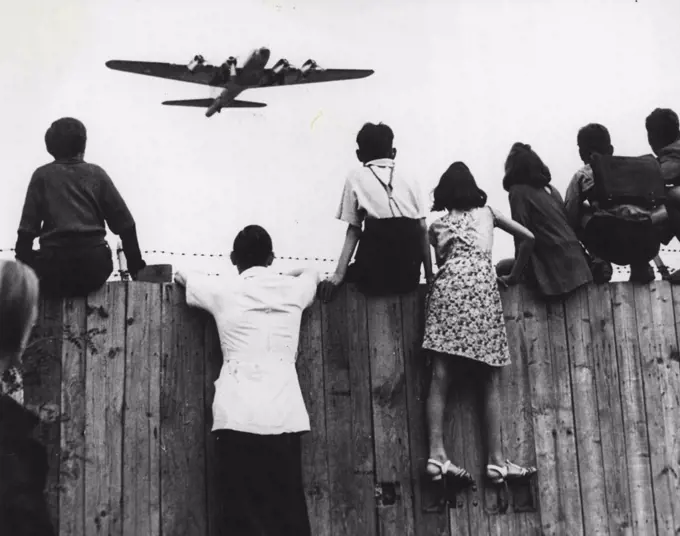 Aircraft Setters At Templehof - Berlin children have a new pastime these days as they gather on the fences around Templehof Airport, Berlin, Germany, watching the fleets of American planes arrive with supplies for the city, now on short rations because of the land and water blockade established by the Russians. An American four- engine transport flies ahead. May 07, 1948. (Photo by AP Photo).