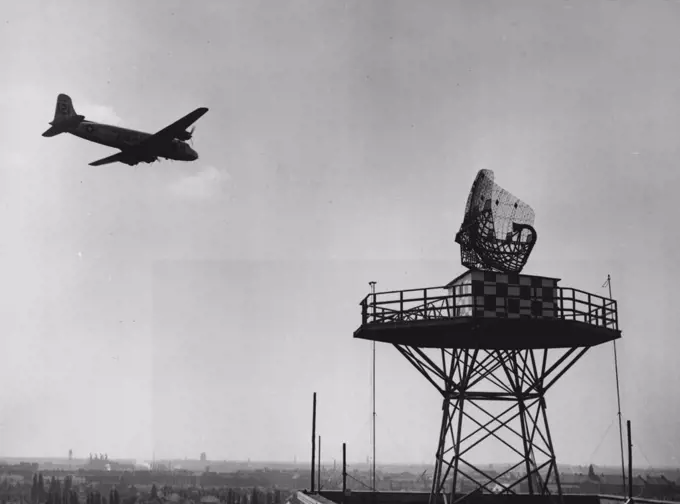 Secret Of The Airlift (First Of Seven) -- A "Vittles" Plane on its return flight to Frankfurt sweeps close by the "Windmill" antenna of the CPS-5. Looking like a against wire marketing basket turned on its side, the antenna whirls round and round. The curved arm (at right) shoots an electronic beam out into space and picks up reflections of that beam as it bounces back from any objects it strikes, in this case, the planes of the airlift. May 06, 1949. (Photo by ACME Newspictures).