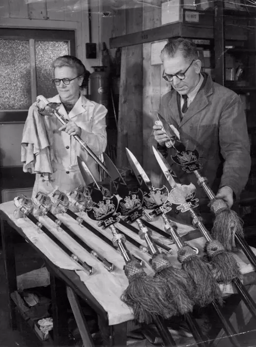 Coronation Weapons Given Their Sparkle by Factory Workers. Mrs. May Fry of Acton polishing swords at the factory, while Mr. Herbert McNab of Fulham, London, foreman sword cutter, cleans some partizans sent from St. James's Palace to be renovated with the new Royal cipher of Queen Elizabeth II. Partizan of this type are carried by the Yeoman of the Guard, Tudor-uniformed Royal bodyguard. A team of craftsmen, and women in a factory at Acton, Middlesex, are now hard at work making 2,000 fine swords for the Coronation. January 24, 1953. (Photo by Reuterphoto).