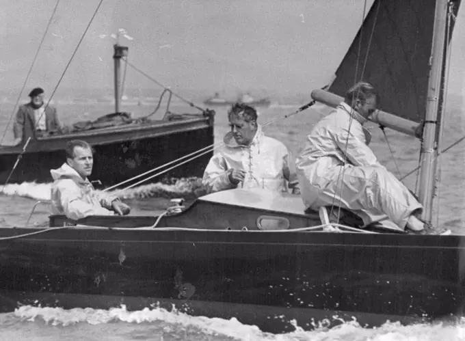 All-round sportsman the Duke of Edinburgh at the helm of the yacht Bluebottle, competing in a race at Cowes Regatta. The Duke is a good cricketer and polo player. On a downwind run at a Cowes regatta, Duke of Edinburgh steers Dragon class Bluebottle which has good chance of winning right to represent at the Melbourne Olympics. Uffa Fox is the burly fellow standing in the cockpit. August 25, 1953.