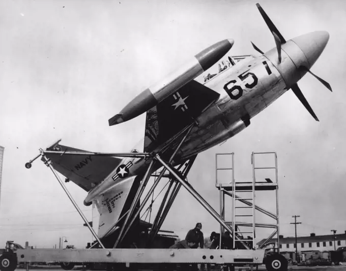 This Plane Will Take Off And Land On Its Tail. - The Plane is moved up to its vertical take off position... This Fantastic New fighter plane, able to take off and land vertically, was Announced recently by the U.S. Navy. Powered by twin Jet Turbines harnessed to contr-Rotating propellers, the XFV-I can take off vertically from a standing start on its tail, level off to fly and fight at very high speeds, and hover stationary in the air and descend for landing on its tail. The plane uses its four-point, X-shaped tail for a landing gear. A specially designed ground handling cart lifts the plane into its vertical take-off position and Also provides the ladder for the the Pilot to Climb up into the cockpit. March 19, 1954. (Photo by Paul Popper Ltd.).