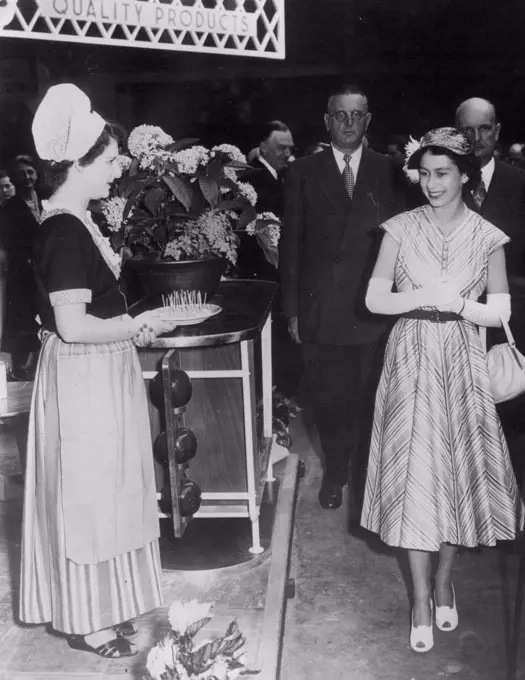 Queen At the Food Fair- Queen Elizabeth, in a cool summer dress and long white gloves, passes a girl in Dutch costume holding a plate of 'tastes' of Dutch cheese, during a private visit to the British Food Fair, Opening at Olympic to-day. July 5, 1952.