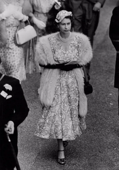 The Queen's Ascot Fashion For Ladies Day -- H.M. The Queen seen walking to the Paddock at Ascot this afternoon. For Ladles Day Her Majesty was charmingly dressed in a filmy white lace dress embroidered overall In fins navy blue braid. Her tiny head hugging forward tilting hat, was to match and The Queen had a fur round her shoulders as protection against the cool breezes. Two outstanding features of her ensemble were the attractive scalloped V neckline of her dress and the extra long handle to her handbag. Today was Ladies Day at Ascot - the third day of the Meeting and several members of the Royal Family, including Her Majesty the Queen were again among the spectators at the Course. June 17, 1954. (Photo by Fox Photos).