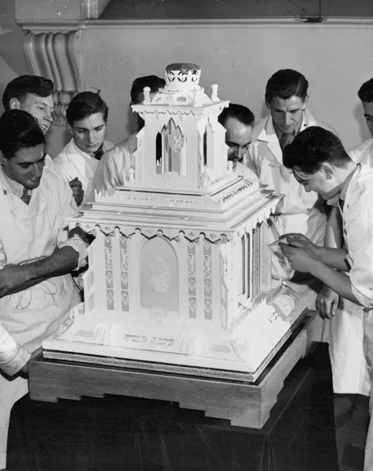 Royal Christening Cake Weighs Over A Hundredweight One of the students at the Borough Polytechnic at work on the cake watched by fellow-students. The front panel depicts a motherhood scene. A christening cake weighing over a hundred weight will by presented to Princess Elizabeth by the National Association of Master Bakers. The cake has been made by students of the National Bakery school, London, who have had only 15 months training. It has one tier, is 36 inches high, and follows traditional liens. Square in design, it is surmounted by a canopy of sugar supporting the Royal Crown. December 09, 1948. 