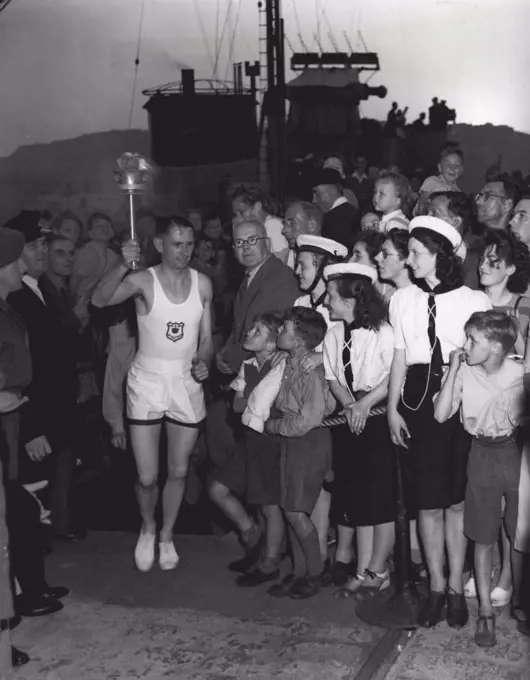 Olympic Flame Reaches Dover : Chief Petty Officer H. Barnes brings the torch Ashore at Dover Pier, The destroyer Bicester in background. July 28, 1948. (Photo by Associated Press Photo).