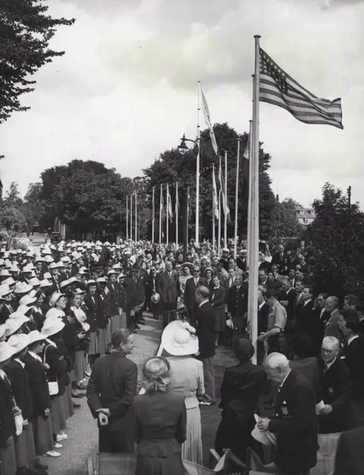 U.S. Flag is Raised At Uxbridge : As the American Flag is secured by a kilted attendant, after being raised by Mrs. Lewis Douglas, wife of the American Ambassador (Third woman from left, back to camera, in foreground), Boery Brundage (standing, centre) president of the American Athletic Association, addresses members of the American Olympic team at the Uxbridge (Middlesex) Camp this morning, July 22. Man standing extreme left (foreground, back to Camera) is the right honourable Lord Burghley, chairman of the organising committee for the Olympic games. Behind him, a little to the right, is Miss Sharman Douglas, daughter of the American Ambassador. July 22, 1948. (Photo by Associated Press Photo).