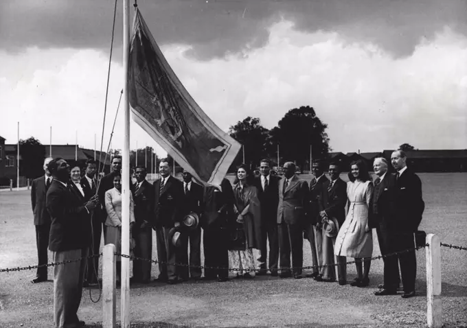 The Above Have Arrived : Newly-arrived athletes from Ceylon watch their team manager, Mr. W. H. D. Perera, unfurling their flag at Richmond Park.A Pleasant little ceremony is being enacted at the Richmond Park Olympic Camp each time a competing team arrives. The visiting athletes stand quietly round whilst their National flag is unfurled. June 21, 1948. (Photo by Fox).