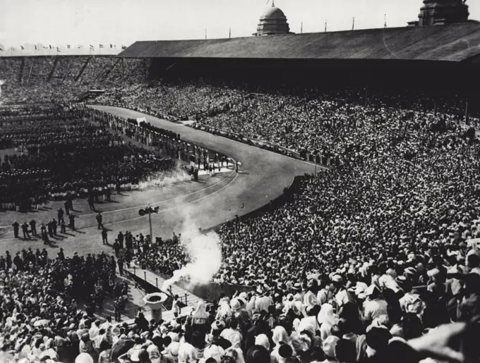 Olympic Fire Blazes At Wembley : Smoke from the torch held by Cambridge "Blue" John Mark drifts up as he is about to kindle the fire which will burn throughout the period of the 1948 Olympic Games. His was the primilege of being the last runner to bear the flame on its hand-to-hand journey from the temple of Zeus in Greece. Watching him in this dramatic ***** the opening ceremony of the 1948 Olympics today, July 29, are 6000 assembled athletes of 58 countries and a crowd of 80,000 packing the sunlit stadium. July 29, 1948. (Photo by Associated Press Photo).