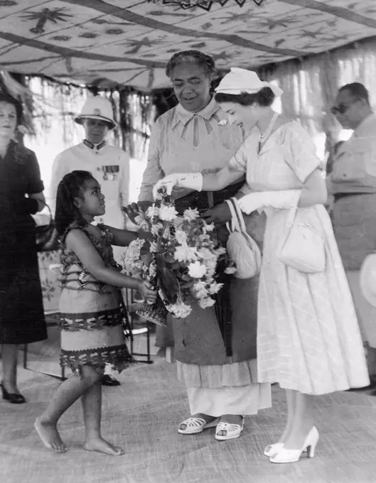 Queen Elizabeth in Tonga - Four year old Mele Siuilikutapu, grand daughter of Queen Salote of Tonga, presents flowers of welcome to Queen Elizabeth. Queen Salote in centre. December 30, 1953.