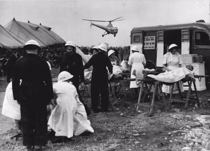 Helicopter Used In Civil: Defense Training Operation -- Nurses and Civil Defense workers dealing with "casualties" at the demonstration this afternoon, while the helicopter which was used to assist in the demonstrations, flies overhead. The Rt. Hone Sir David Maxwell Fyfe, Q.C. M.P. Secretary of State for the Home Department, today opened the Bully Fen Rescue Training Ground at Hackney, East London, after which demonstration was given by members the Civil Defence Services. April 15, 1953. (Photo by Fox Photos).