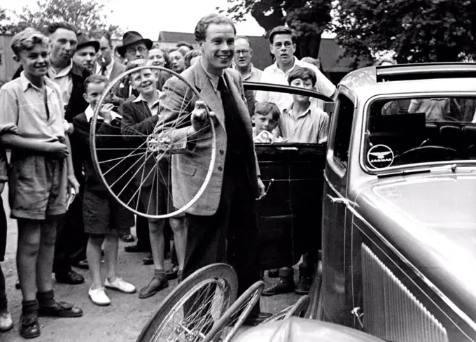 British Champion Still Hope To Race -- A smile on his face, a cycle wheel in his hand and with a girl friend In his car, Reg Harris, world cycling sprint champion, dropped from Britain's Olympic team, arrives at Herne Hill track. "I have not given up hope of representing my country", he said. August 05, 1948. (Photo by Mirror Features).