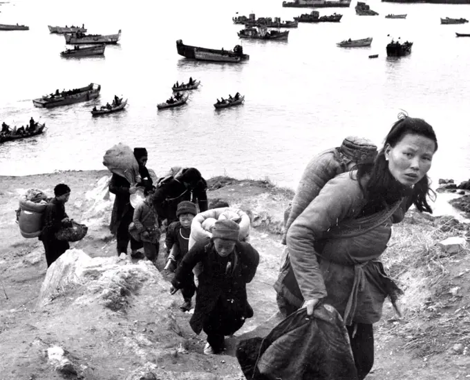 A line of Tachen refugees climb over a hill to reach their designated embarkation point. In the background native sampans are used during low tide to carry evacuees to landing craft. February 18, 1955. (Photo by United Press).