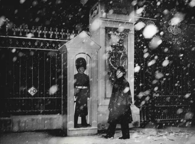 His Regiment Has Just Returned From Malaya - A policeman wales past the sentry in his box outside Buckingham Palace, today Dec 4th, at 3.30 p.m., during London's first heavy fall of snow.The guard is of the 2nd battalion coldstream guards, which has just returned from service in Malaya, and is now carrying out guard duty at the Palace. December 4, 1950. (Photo by Associated Press Photo).
