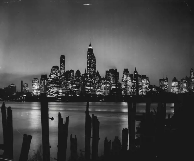Manhattan Mazda (Tenth Of Eleven) -- Office buildings in the busy downtown financial district of Manhattan are still aglow at dusk. Forgotten pilings at a Brooklyn wharf from a weird contrast to the throbbing commercial center, viewed across North River. May 12, 1952. (Photo by United Press).