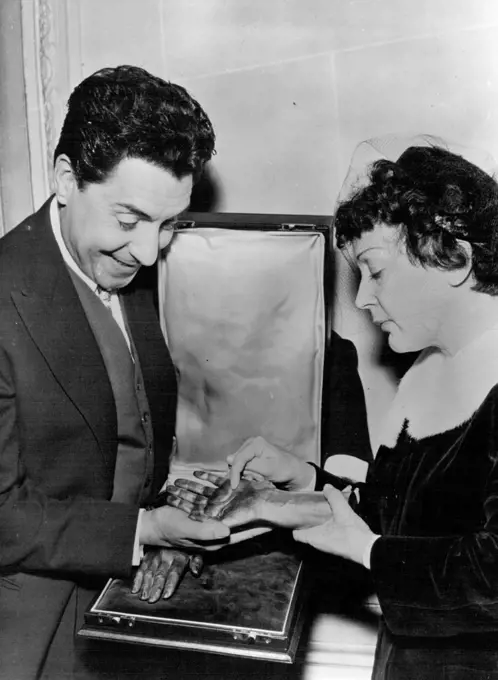 A Hand In Celebration -- Edith Piaf with husband Jacques Pills as they admire their unusual Anniversary gift. Singer Edith Piaf Celebrated Her first wedding anniversary in Paris yesterday.At the Champs-Elysees Pavilion Edith was Presented a Bronze cast of her hands. The presentation was made by the her recording company. The Bronze hands were made by the Chiroteque Francais. January 5, 1954. (Photo by Paul Popper, Paul Popper Ltd.).