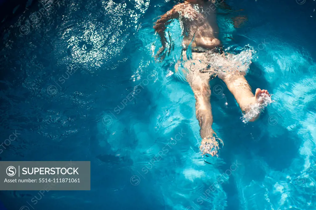 Boy 7-8 years old kicks in pool water during summer time