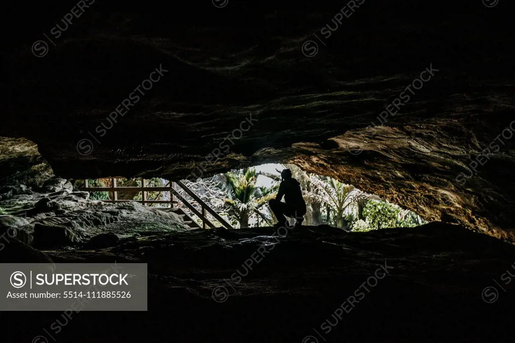 A woman in silhouette kneels at the entrance to a cave in New Zealand