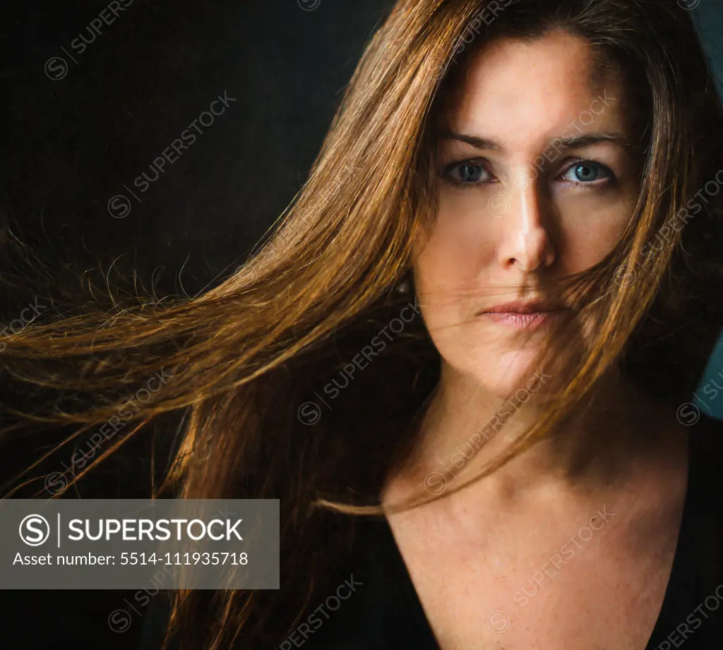 Portrait of a woman with long brown hair blowing across her face.