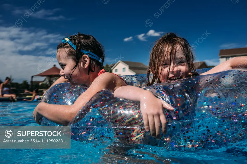 happy girls playing in pool float together while swimming