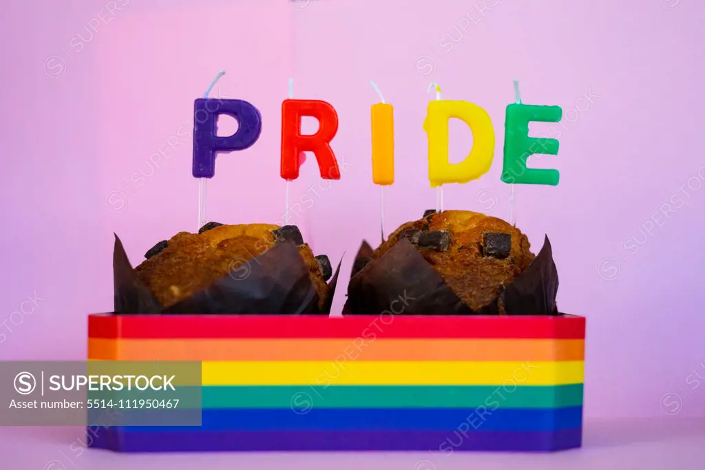 Two muffins with candles and Pride flag.