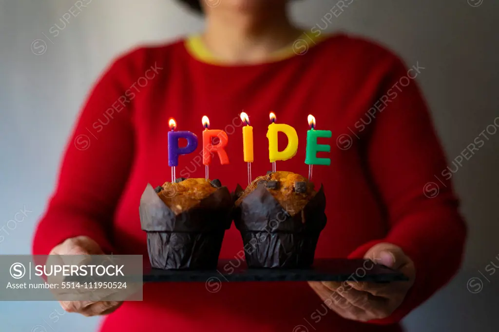 Woman picking up a plate with muffins and Pride candles.