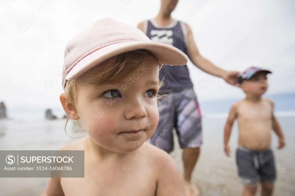 Portrait of cute one year old girl at the beach with brother and dad.