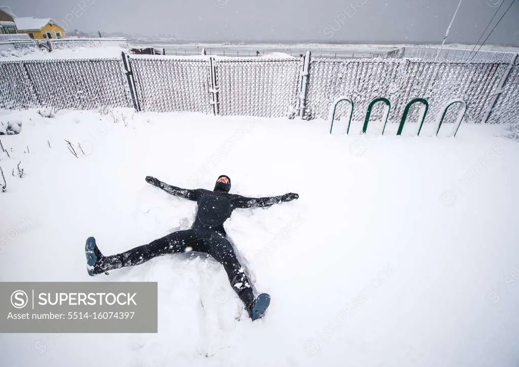 Surfer making snow angel on beach in Maine during Nor'easter storm