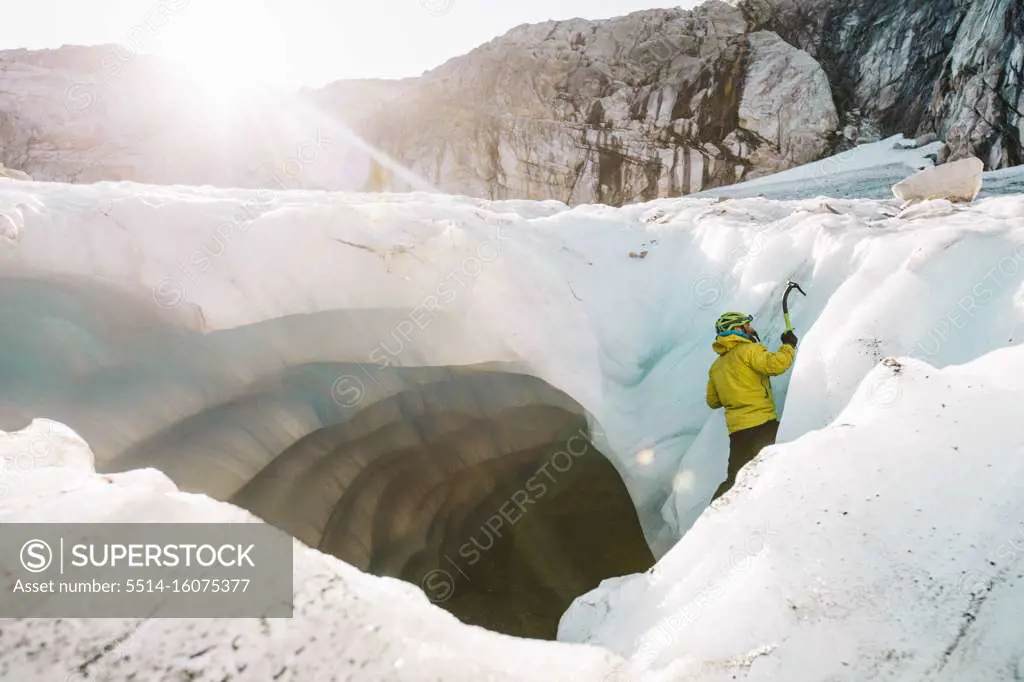 Side view of man ice climbing outside of glacial cave.