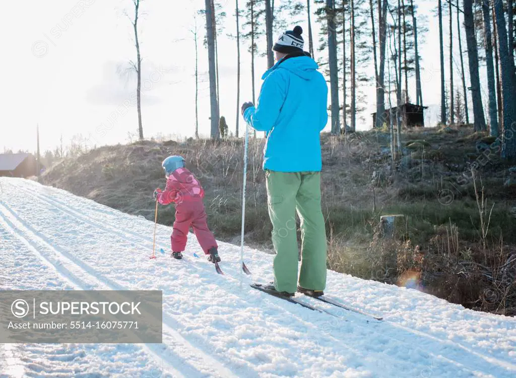 young girl cross country skiing with her dad in Sweden at sunset