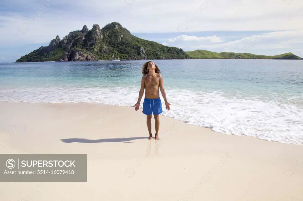 One male tourist, wearing blue swuimsuits, meditating on idyllic beach