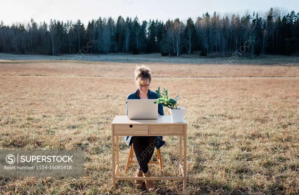 travelling woman working on a laptop and desk in a field outside