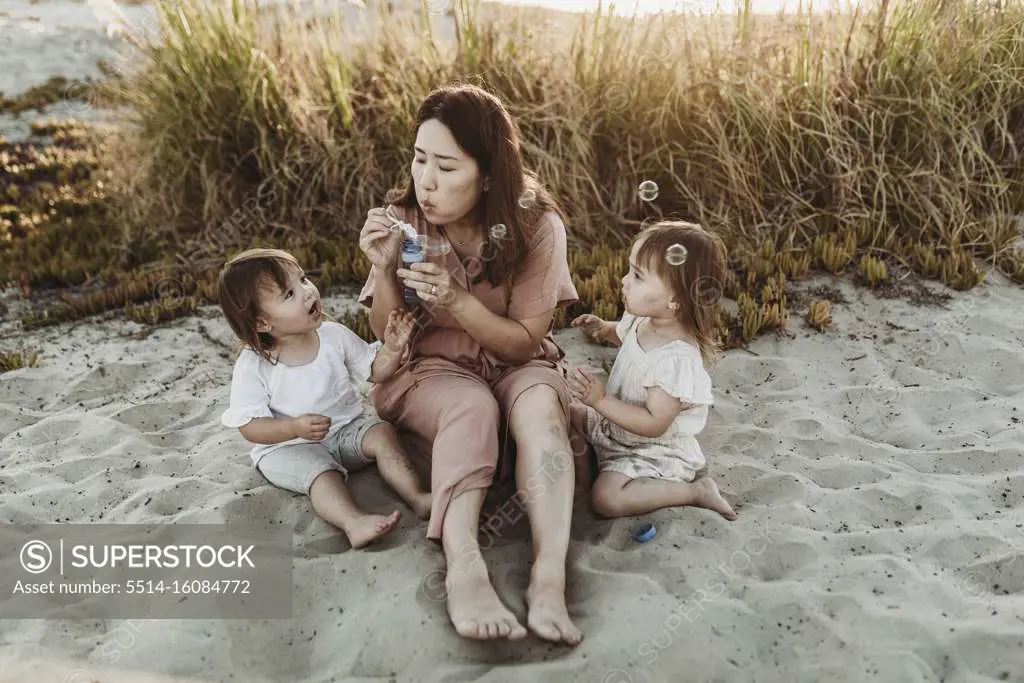 Mother with young twin daughters blowing bubbles at the beach