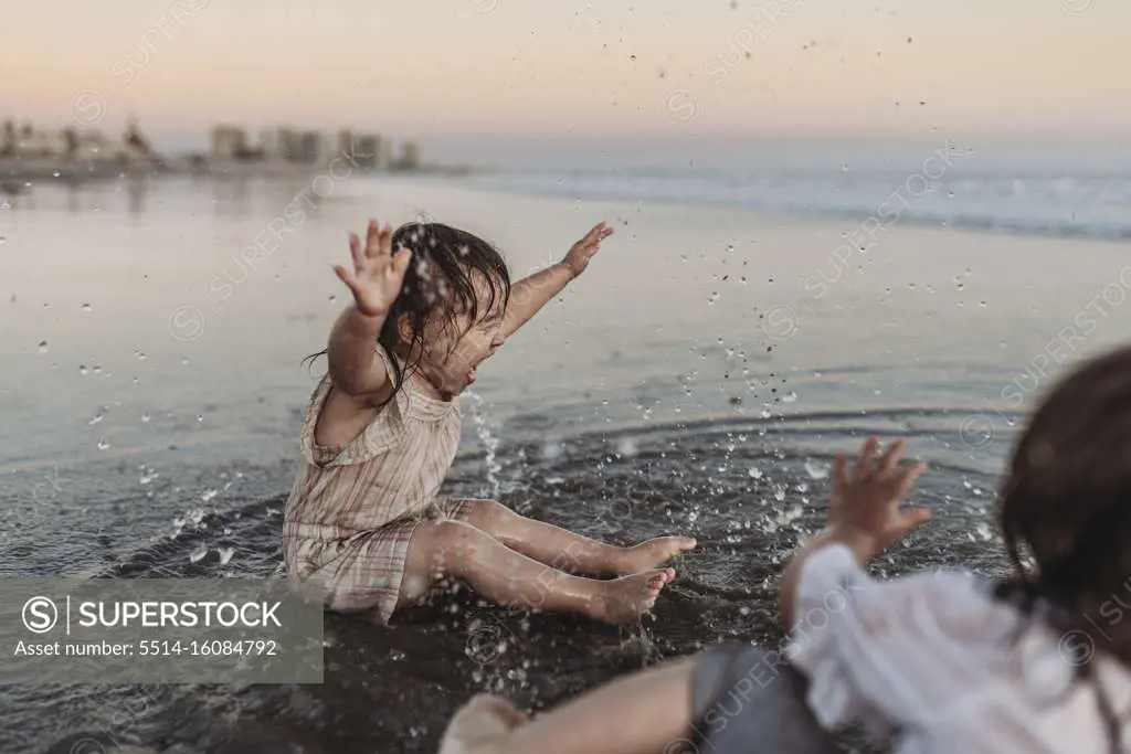 Happy 2 year old girl splashing in ocean water at beach