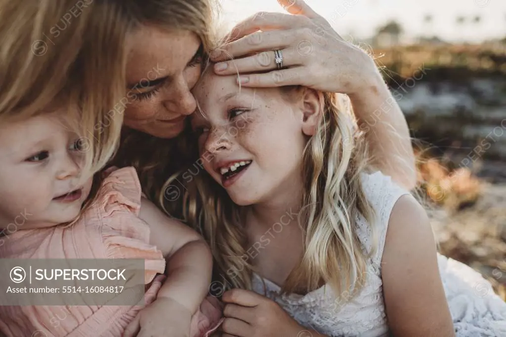 Portrait of mother cuddling with young daughters at beach sunset