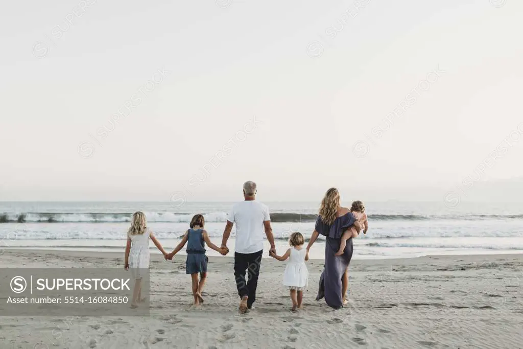 Behind view of young family walking towards the ocean at sunset