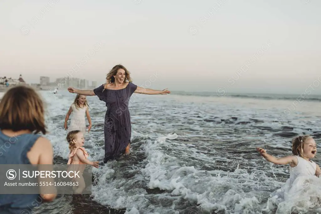 Strong mother with four daughters playing in ocean at sunset